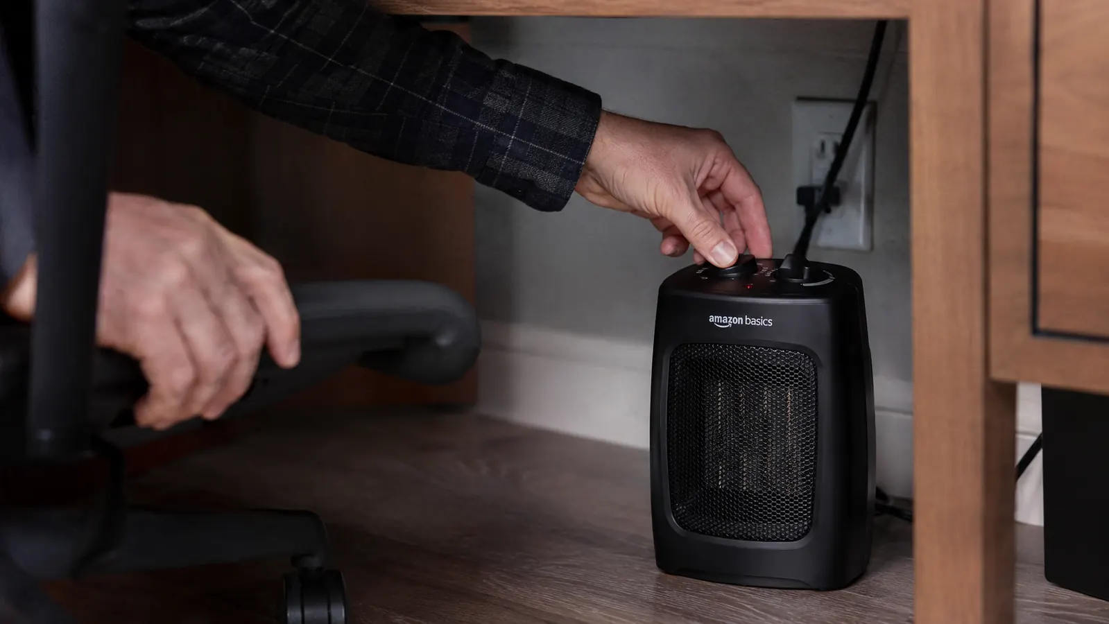Close-up of a hand plugging in and switching on the Amazon Basics ceramic mini space heater under a desk