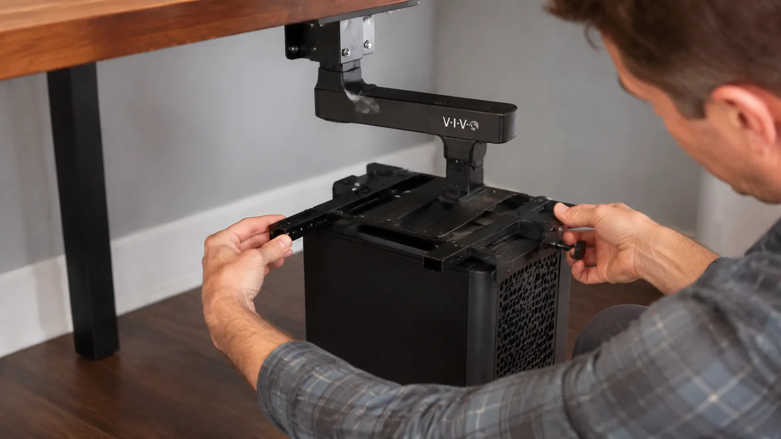 Close-up of a hand sliding the width bracket on a VIVO under-desk CPU mount before tightening it around a computer tower